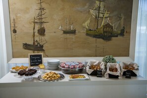 A buffet table with various pastries and desserts, a chalkboard sign, and a maritime painting in the background. - Hotel Mon Cheri (Riccione)