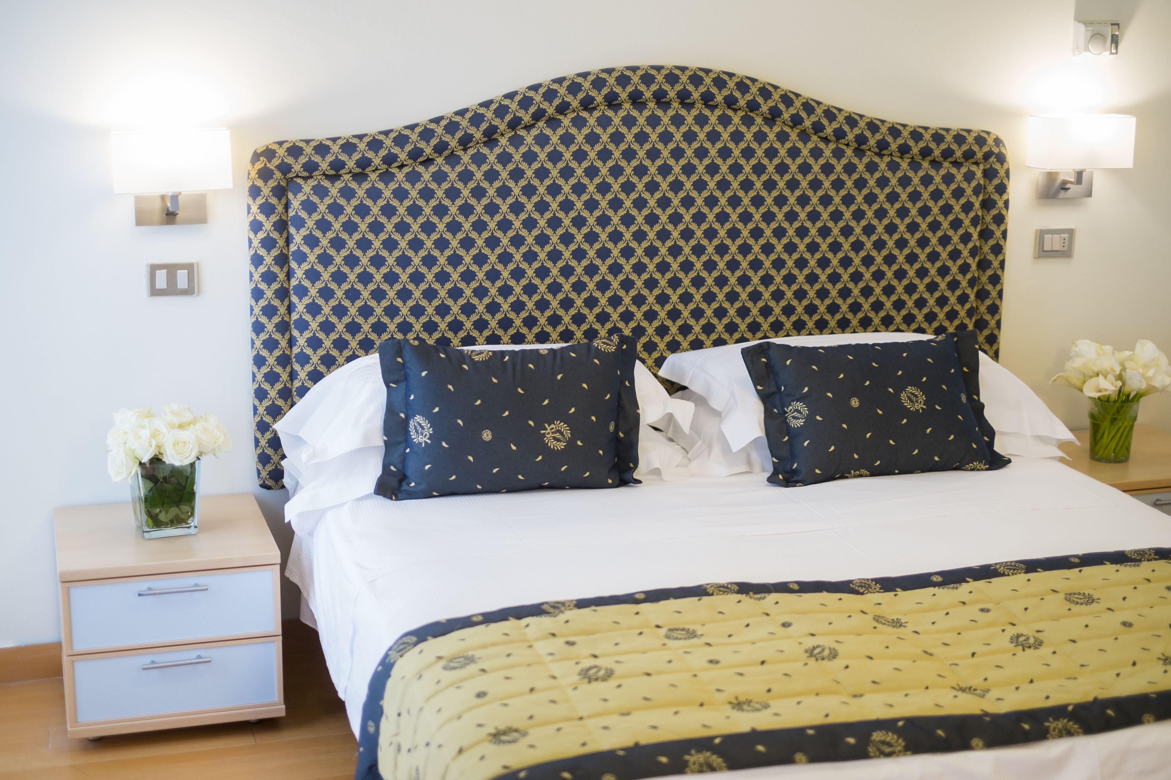 Un lit bien fait, avec une tête de lit à motifs, une literie blanche et des coussins décoratifs.