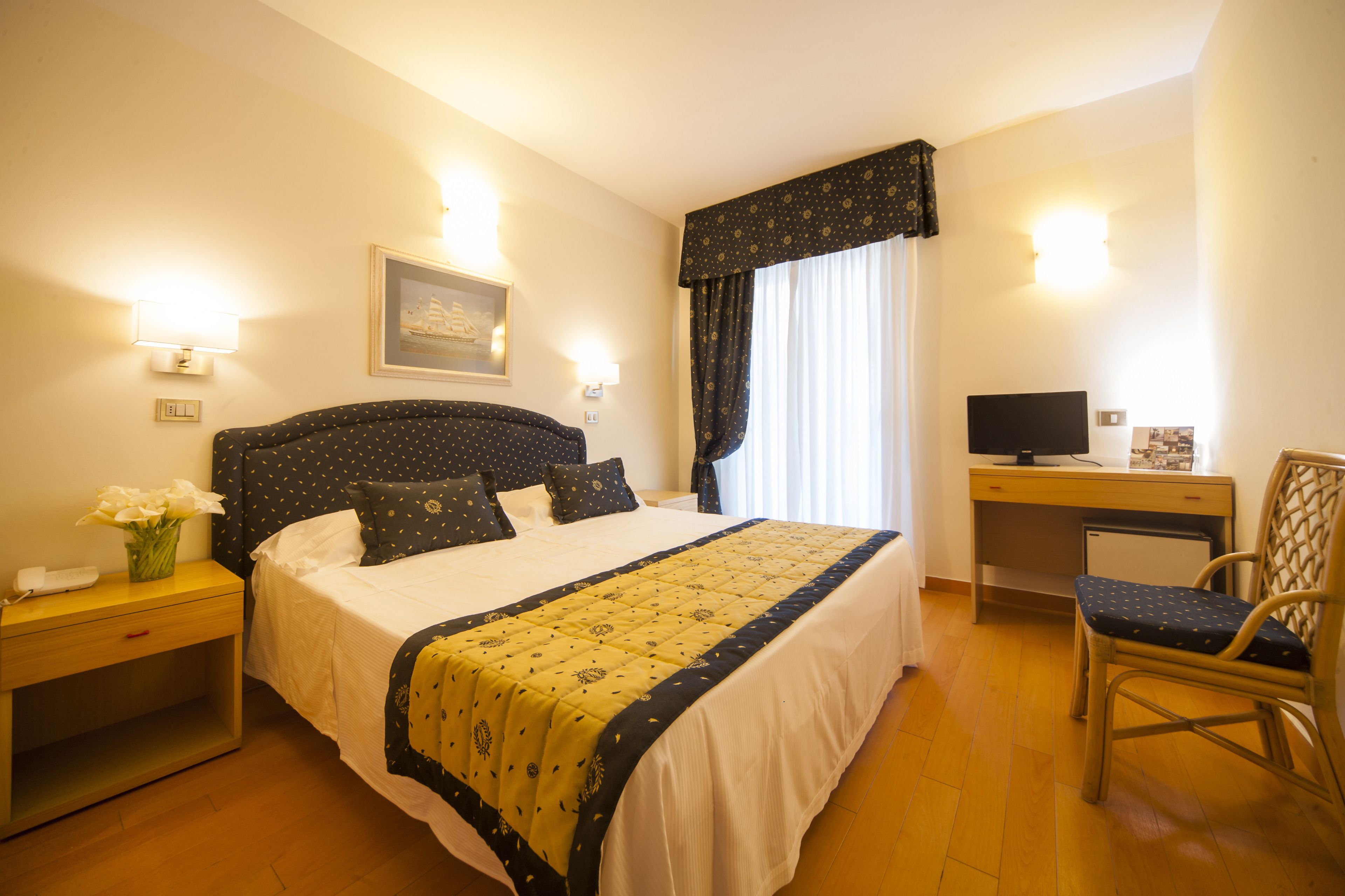 A neatly arranged hotel room with a bed, bedside table, chair, desk, and a small TV.