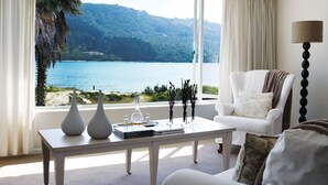 Uma sala de estar moderna com vista para um lago e montanhas, um sofá branco, uma mesa de centro com objetos decorativos e um abajur.