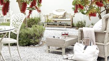 A wicker lounge area with a bench, a small table, and a chair. There are two glasses of red wine on the table.
