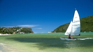 Veleiro com o número 90855 em um dia claro em uma praia, com casas ao fundo.