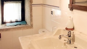 A bathroom with a marble sink, a mirror, and a window with a curtain.