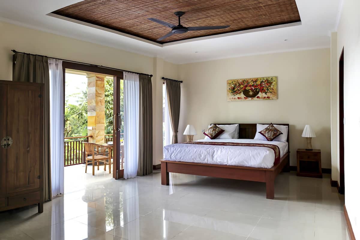 Un dormitorio amplio con una cama grande, ventilador de techo y vistas al exterior mediante una puerta corrediza.