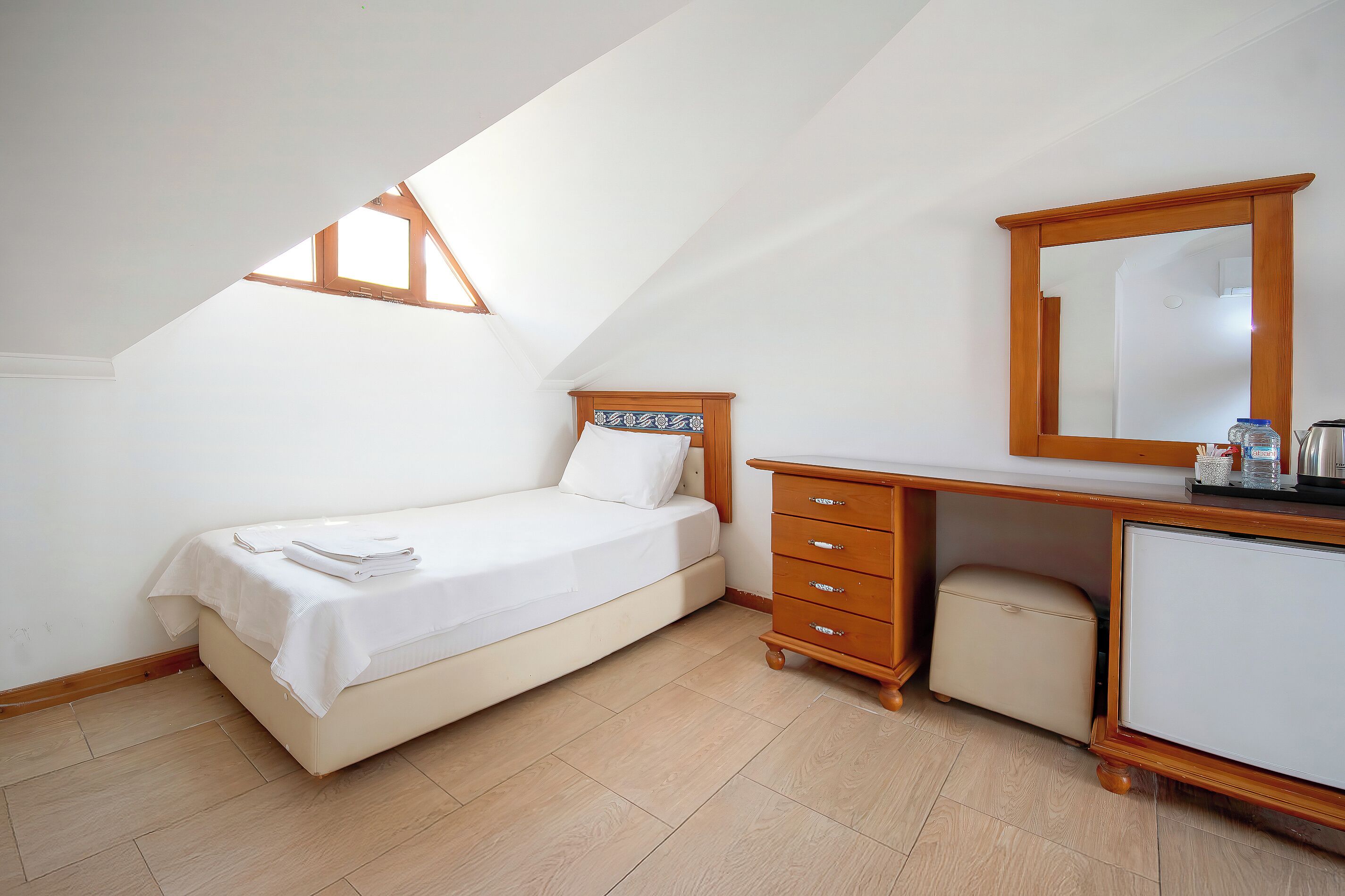 Ein Schlafzimmer mit Bett, Kommode, Spiegel und Dachfenster.