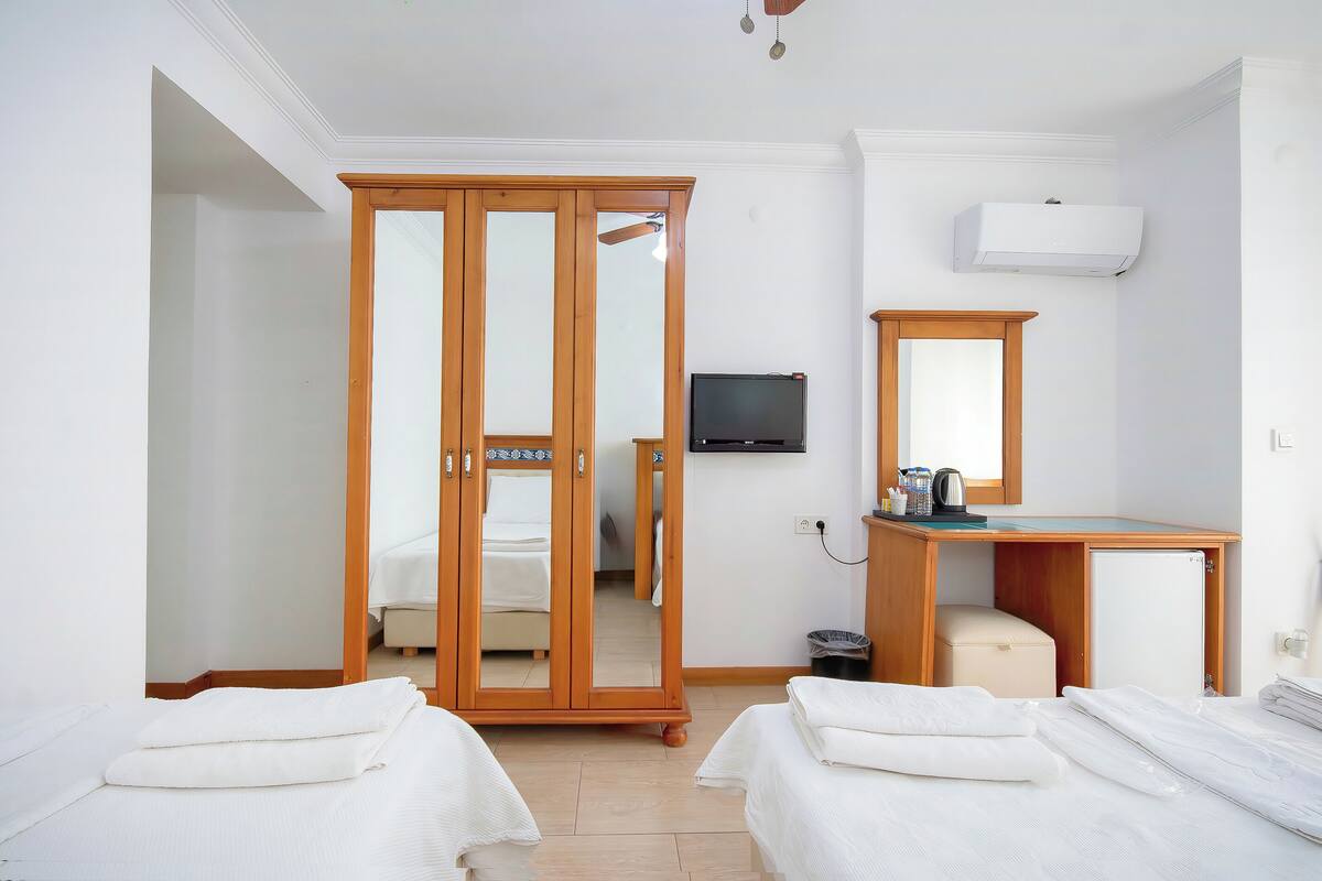 A hotel room with two beds, a wooden wardrobe, a desk with a mirror, a television, and an air conditioning unit.