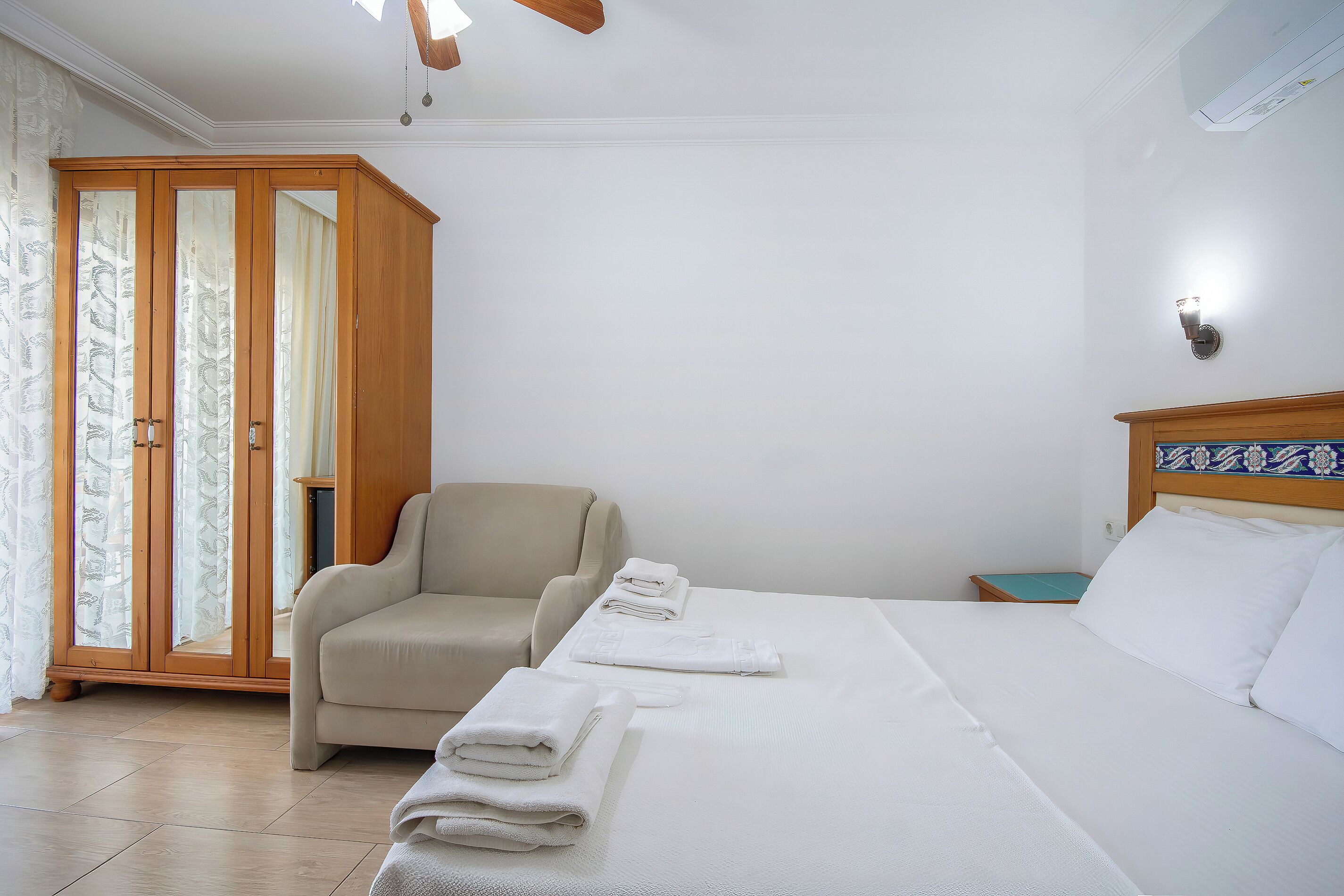 A hotel room with a bed, a chair, a wardrobe, and a nightstand.