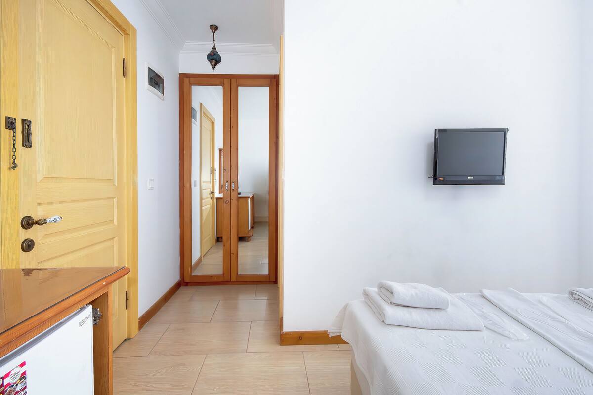 A bedroom with a bed, a TV mounted on the wall, and a wooden door.