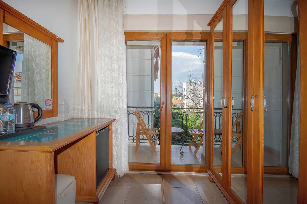A room with a wooden desk, a television, and a view of a balcony with outdoor furniture.