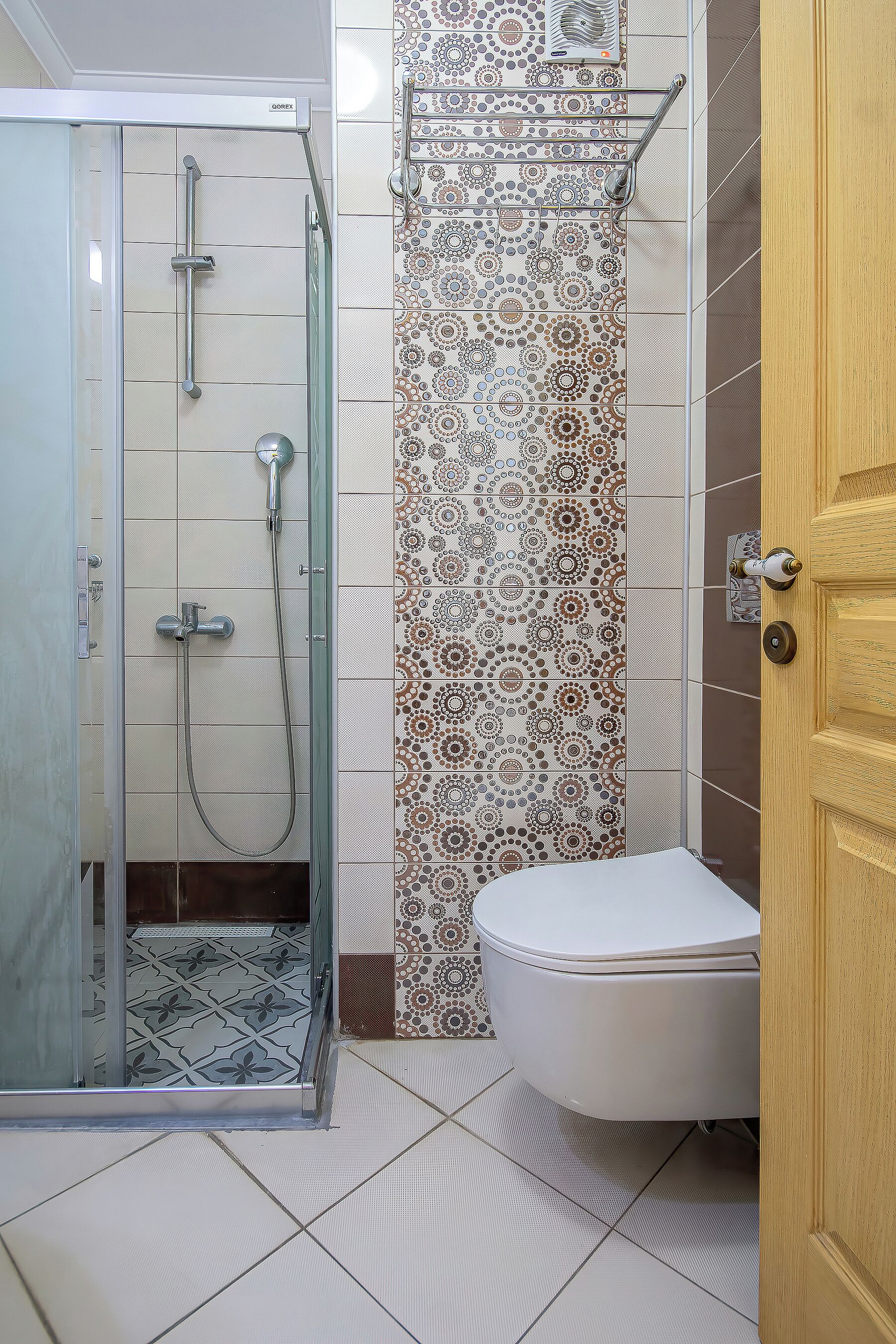 A bathroom with a glass-enclosed shower, a toilet, and patterned tiles.
