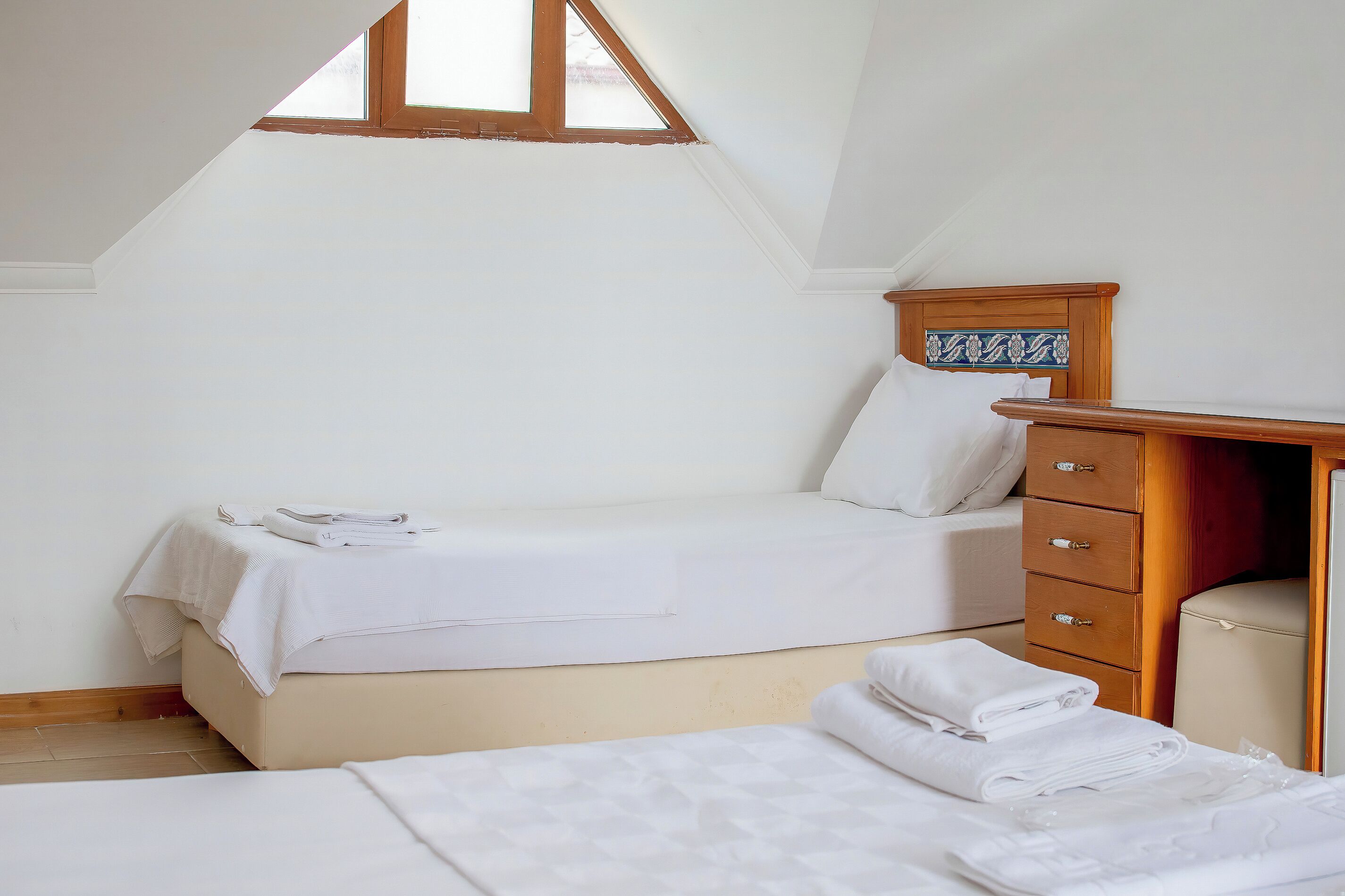 A bedroom with two beds, a wooden dresser, and a skylight.