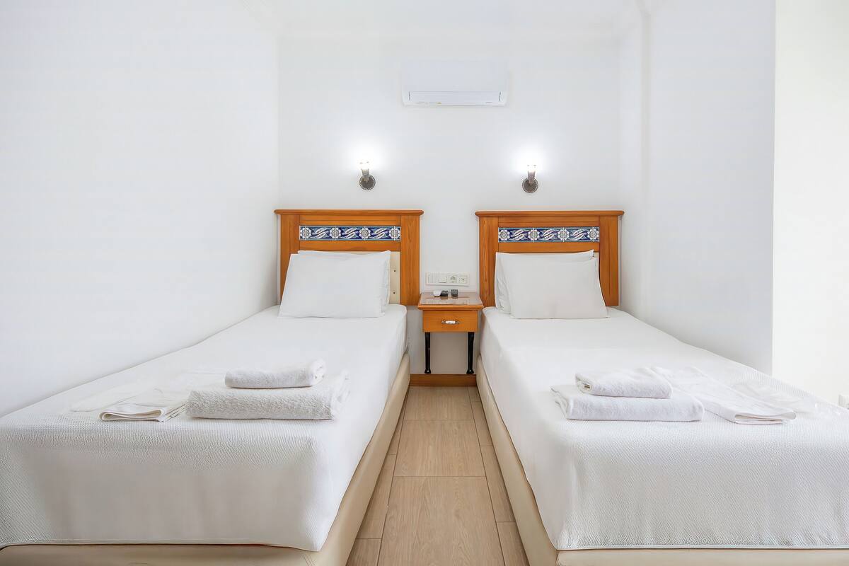 A twin room with two single beds, each with a wooden headboard, white bedding, and a nightstand with a lamp.