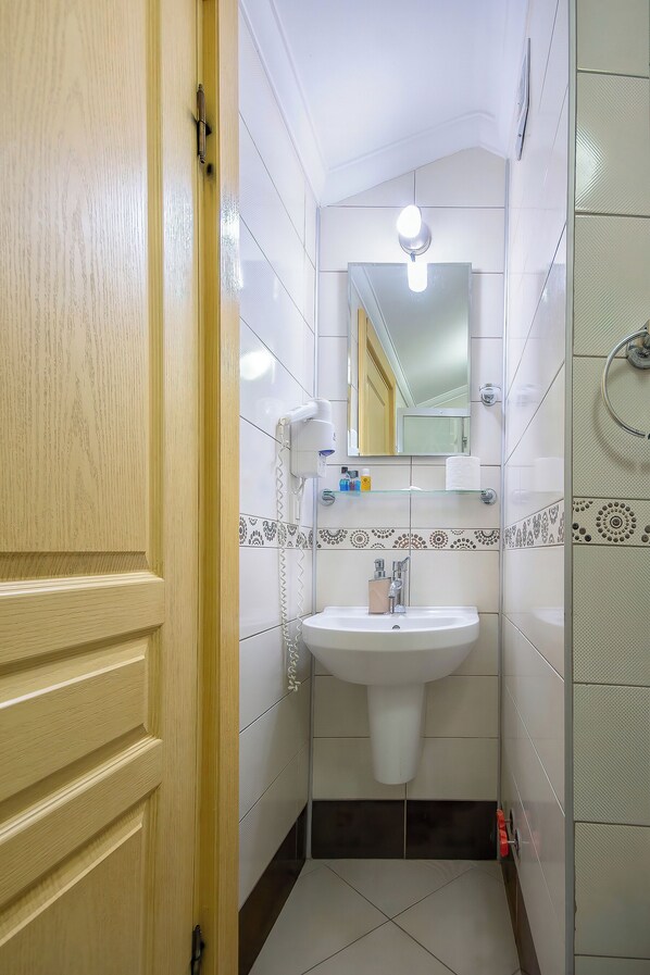 A bathroom with a wooden door, a white sink, a mirror, and a shower area.