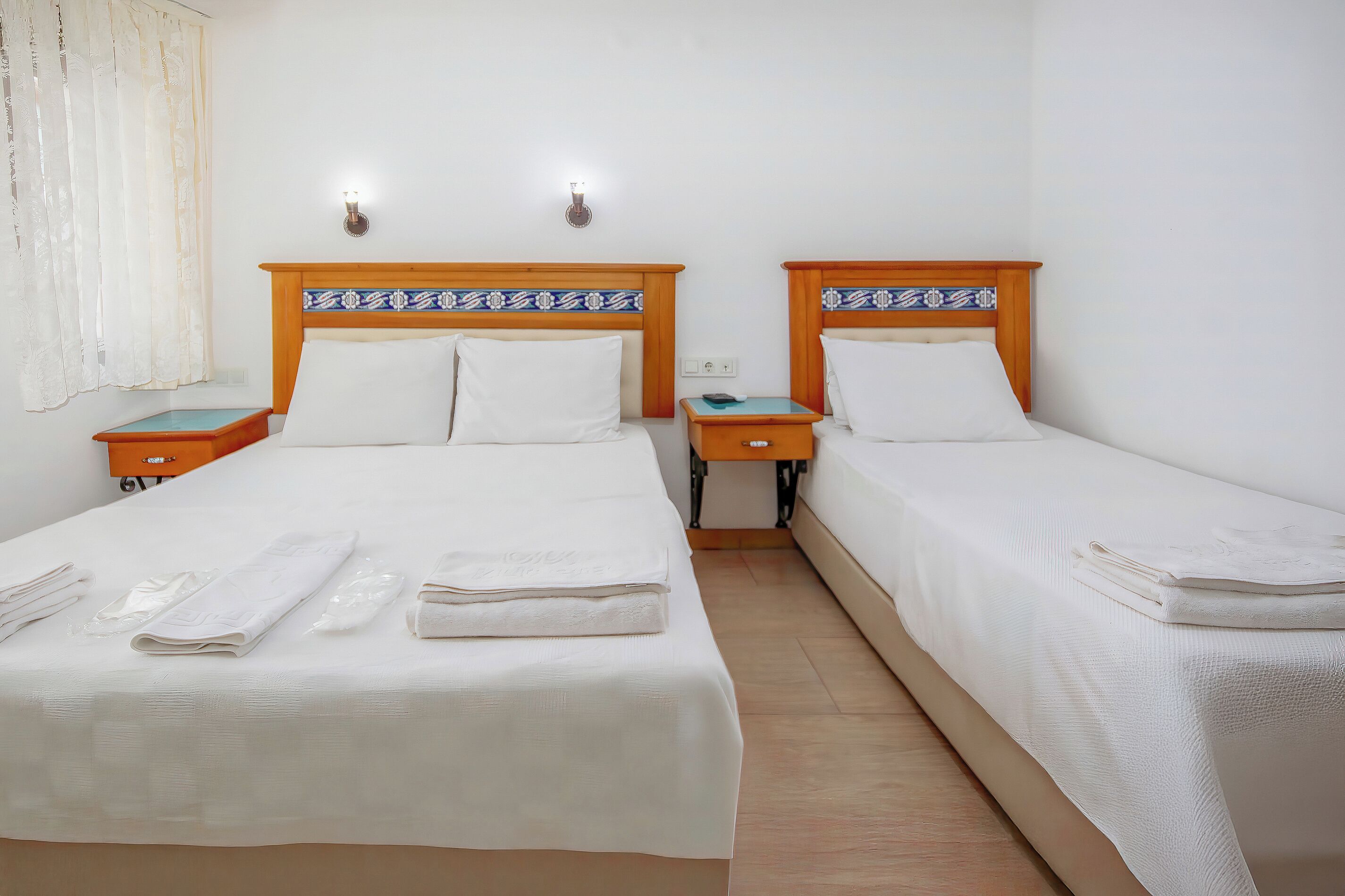 A hotel room with two beds, each with a wooden headboard and white bedding. There are two bedside tables, one on each bed, and a nightstand between them.