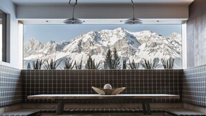 Un interior moderno con un banco y una mesa frente a un ventanal con vistas a una cadena montañosa.