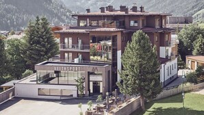 Un edificio moderno de varios pisos con restaurante e instalaciones deportivas en la planta baja, rodeado de montañas y árboles.