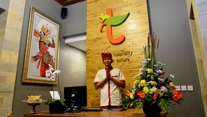 A reception desk with a framed artwork, a wooden wall with a logo, and a floral arrangement. - Tetirah Boutique Hotel Ubud (Ubud)