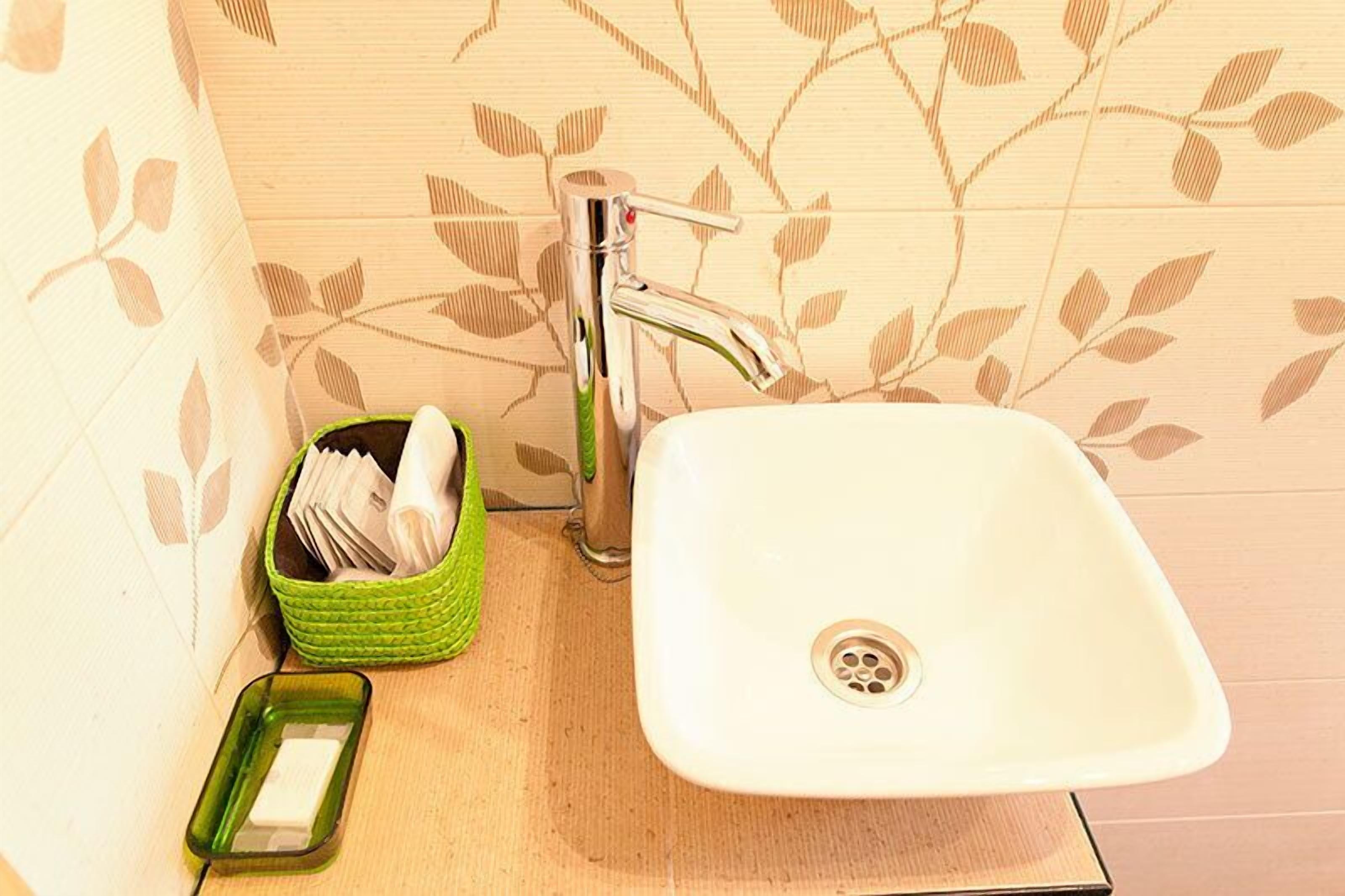 A bathroom with a white sink, a green soap dish, and a green basket containing toiletries.