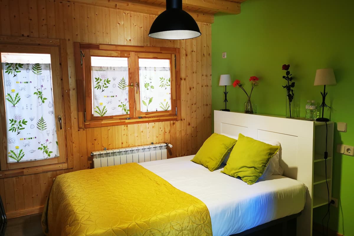 Una habitación con paredes de madera, una cama con ropa de cama amarilla, un radiador y una ventana con cortinas florales.