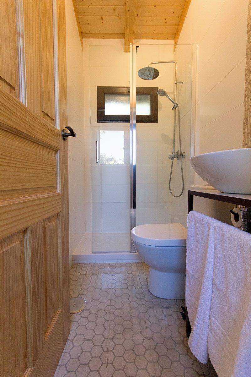 Une salle de bain avec une porte en bois, des toilettes, une douche avec une porte en verre et un lavabo avec une serviette.