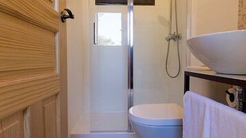 Une salle de bain avec une porte en bois, des toilettes, une douche avec une porte en verre et un lavabo avec une serviette.