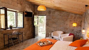 Um quarto aconchegante com parede de pedra, cama com roupa de cama laranja, mesa de jantar com bandeja de comida e uma cadeira.