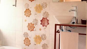 Un baño con una bañera blanca, un tocador de madera con un lavabo, un espejo y un papel tapiz floral.