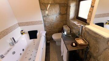 A bathroom with a stone wall, a glass-enclosed sink, a white bathtub, and a toilet.