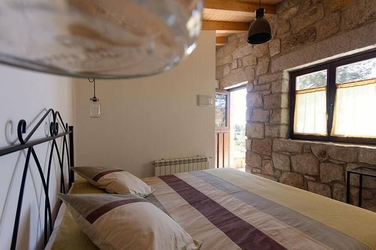 Un dormitorio con pared de piedra, una cama con colcha a rayas, un radiador y una lámpara colgante.