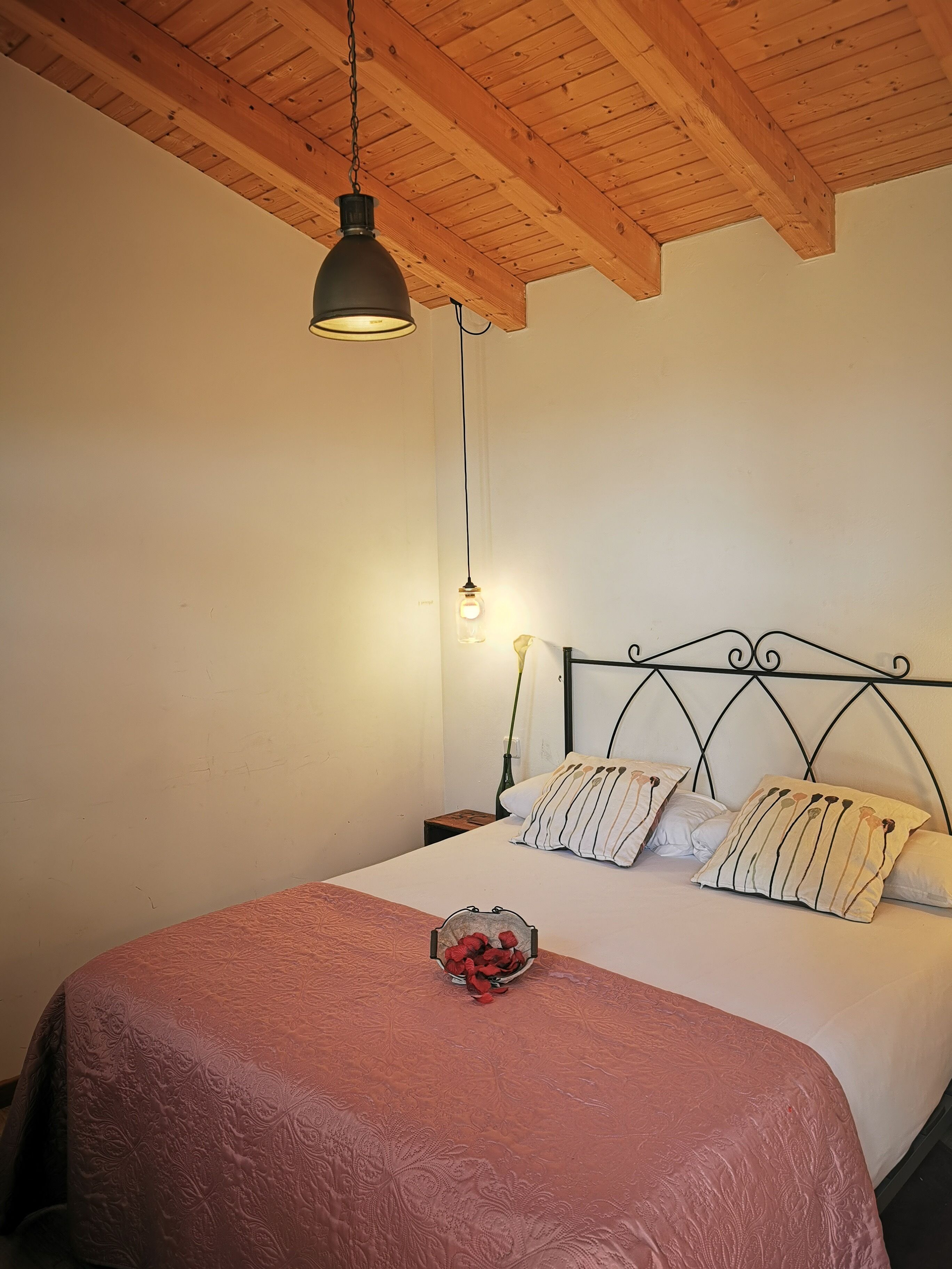 Una camera da letto con soffitto in legno, un letto con copriletto decorato e un comodino con un vaso di fiori.