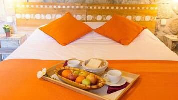 A neatly made bed with orange pillows and a tray of fruit and bread.