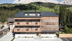 Un hotel con fachada de madera, balcones con jardineras y vistas a montañas al fondo.