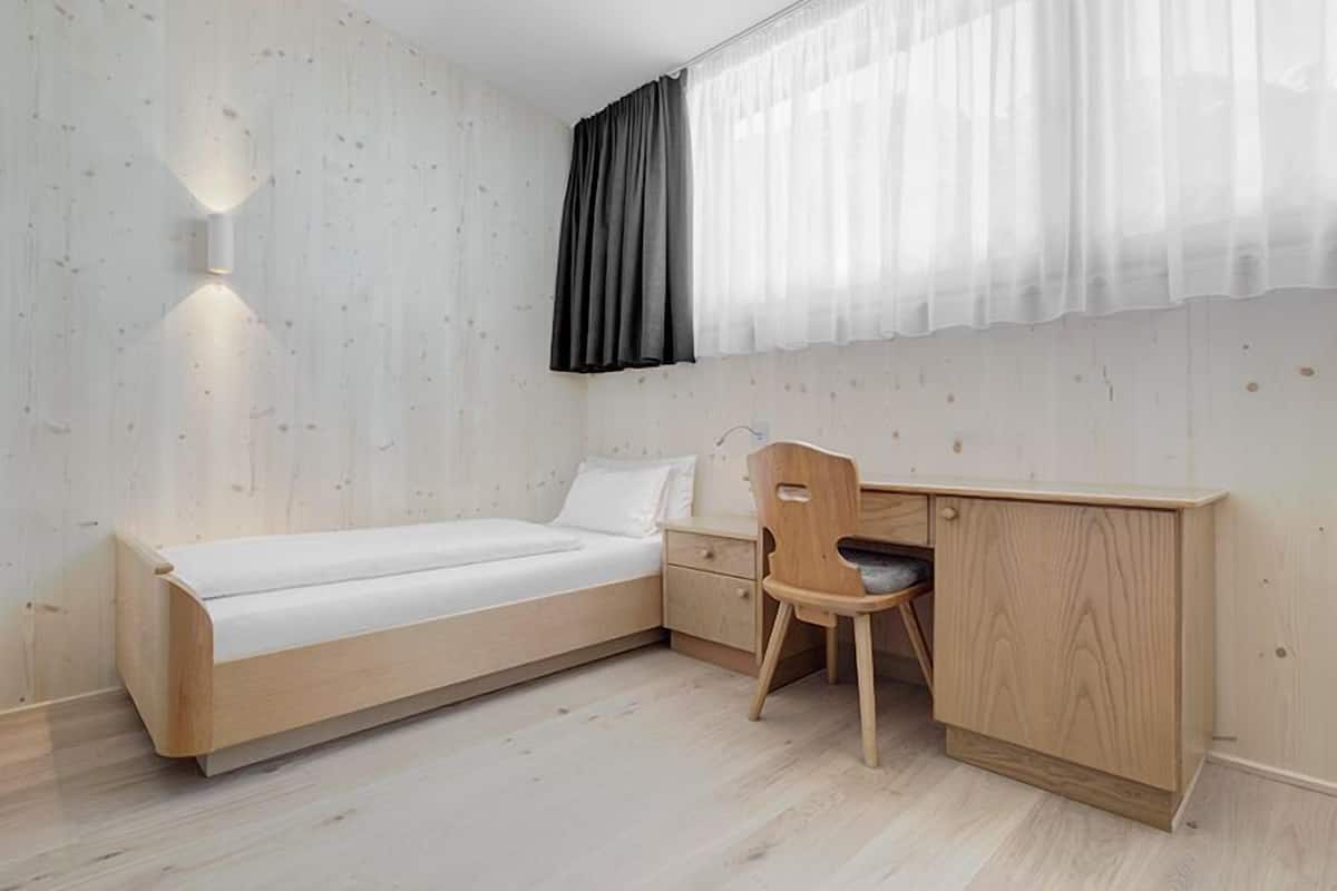 A minimalist bedroom with a wooden bed, a desk, and a chair.