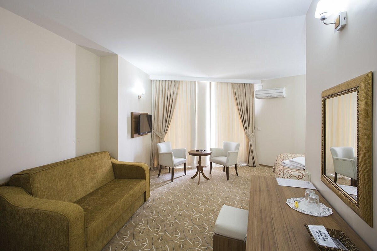 Ein Hotelzimmer mit einer Couch, zwei Stühlen, einem kleinen Tisch, einem Spiegel und einem Bett.