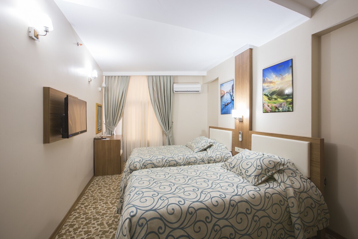 Ein Hotelzimmer mit zwei Betten, einem Flachbildfernseher, einer Klimaanlage und zwei gerahmten Bildern an der Wand.