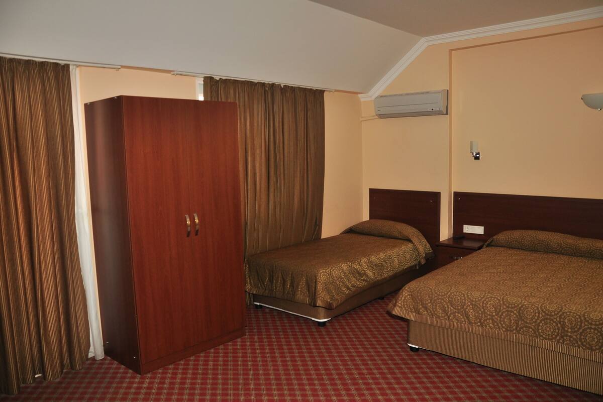 A hotel room with a wardrobe, two single beds, a red checkered carpet, and an air conditioning unit on the wall.