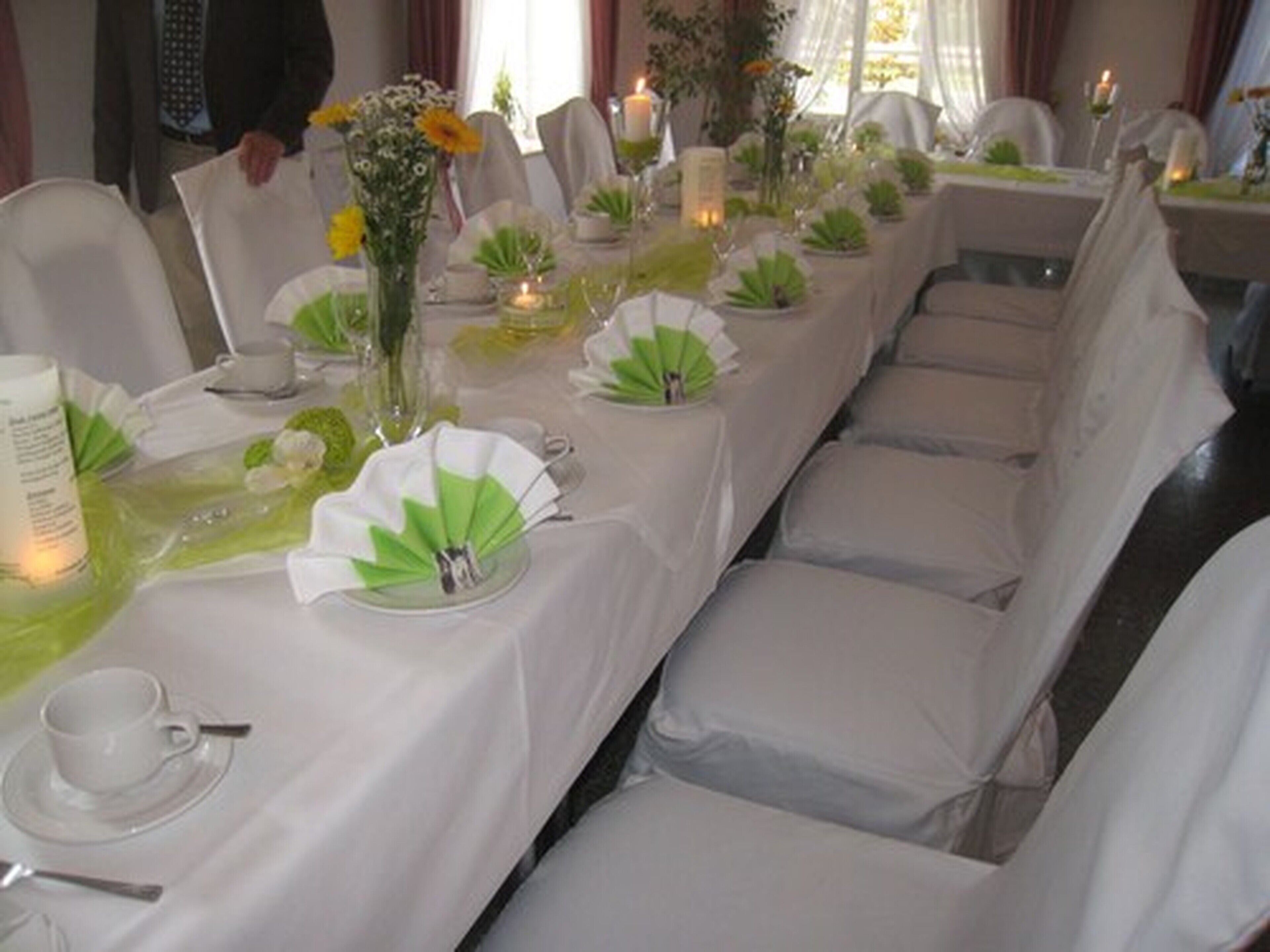 Une table de banquet dressée avec des nappes blanches, des décorations florales vertes et des bougies.