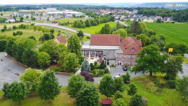Vue aérienne d’une ville avec un bâtiment remarquable, reconnaissable à son toit rouge, entouré de verdure et bordé d’un parking.