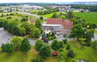 Ett flygbildsbild av en stad med en framträdande byggnad med rött tak, omgiven av grönska och ett parkeringsområde.