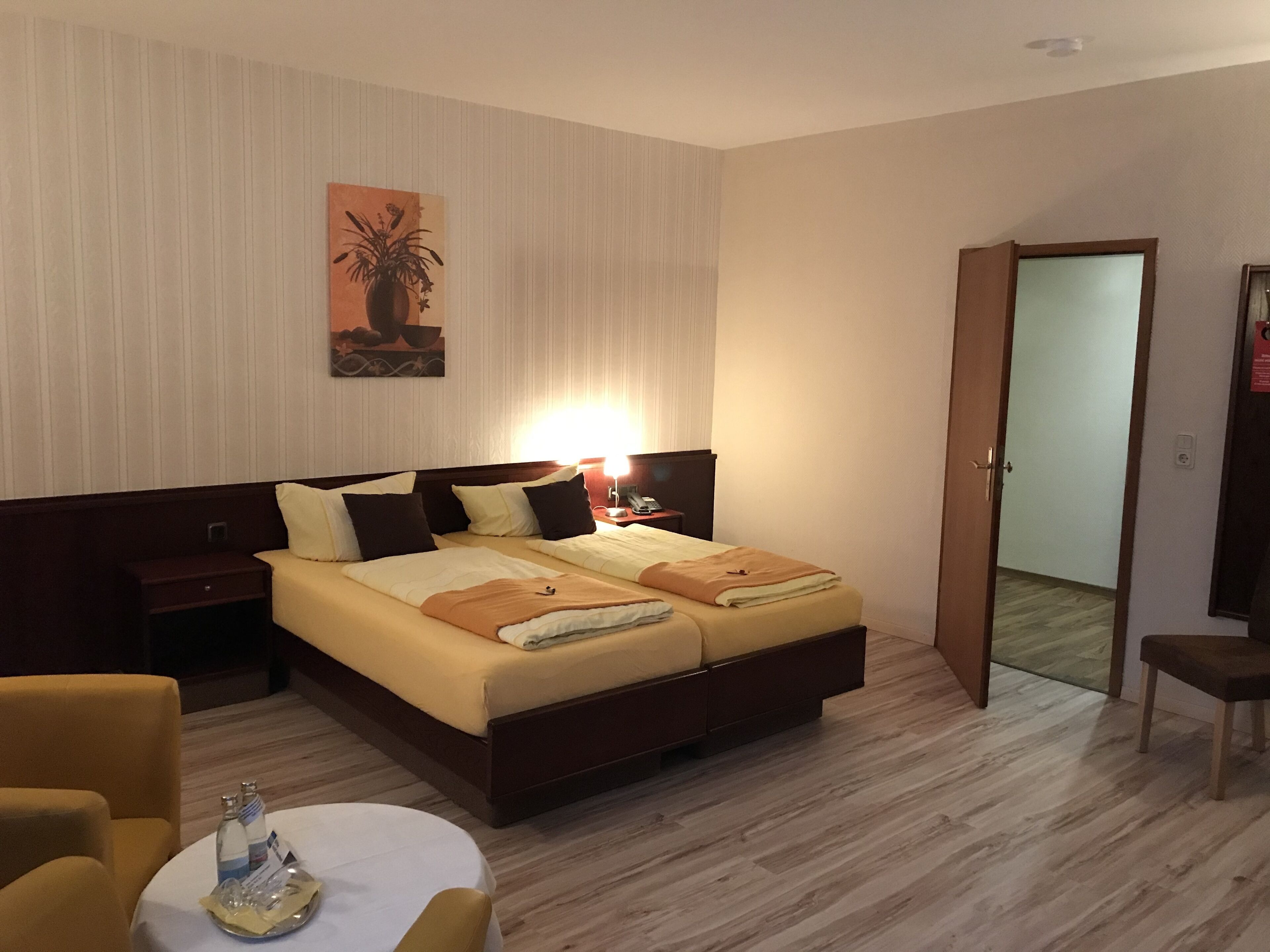 Quarto de hotel com cama, mesas de cabeceira, abajur, cadeira e um quadro na parede.