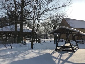 A snow-covered outdoor area with a wooden pavilion, benches, and bare trees. - Hotel Schöne Aussicht (Weissenfels)