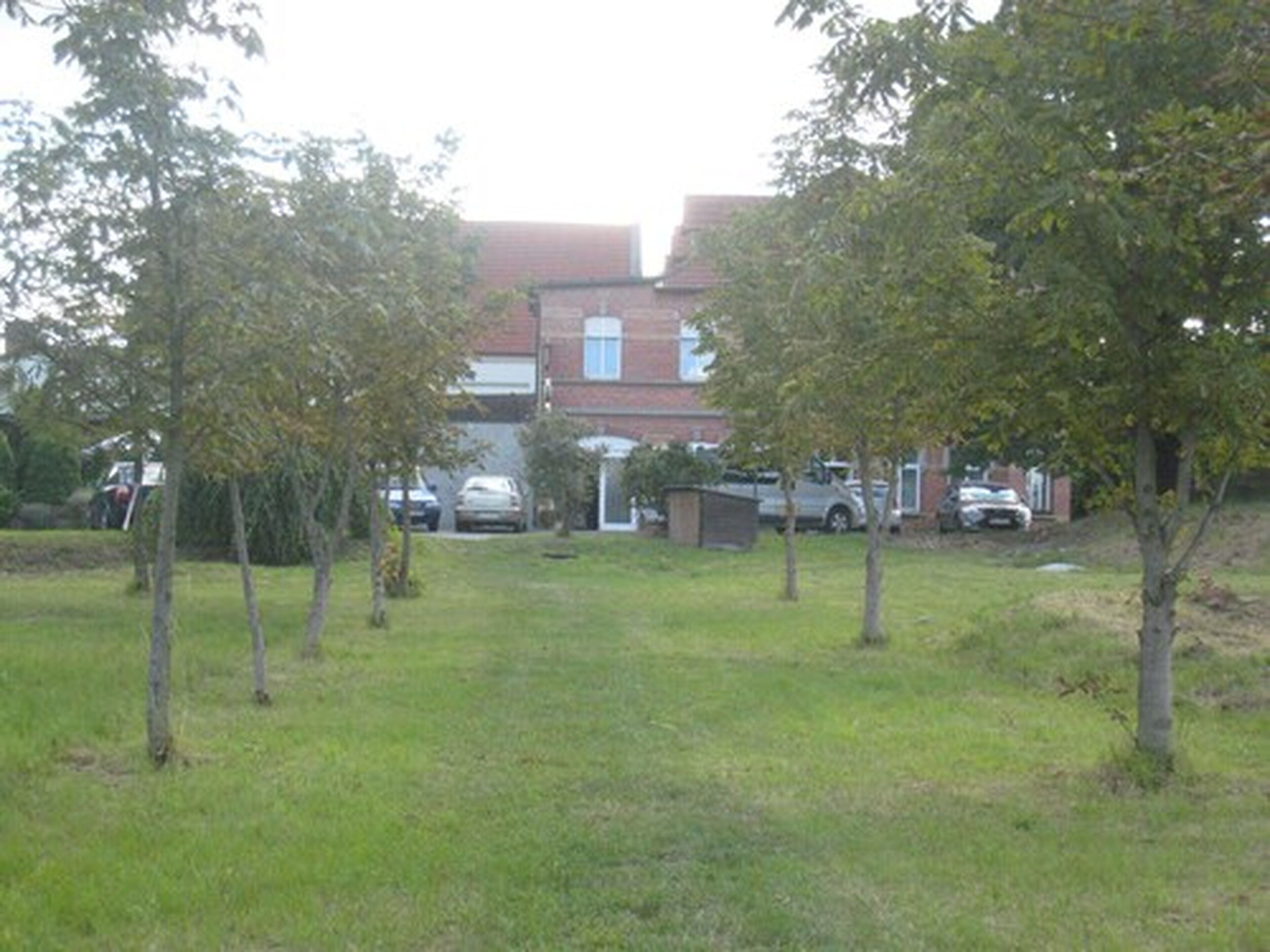 A residential area with a brick house, a small garden, and parked cars.