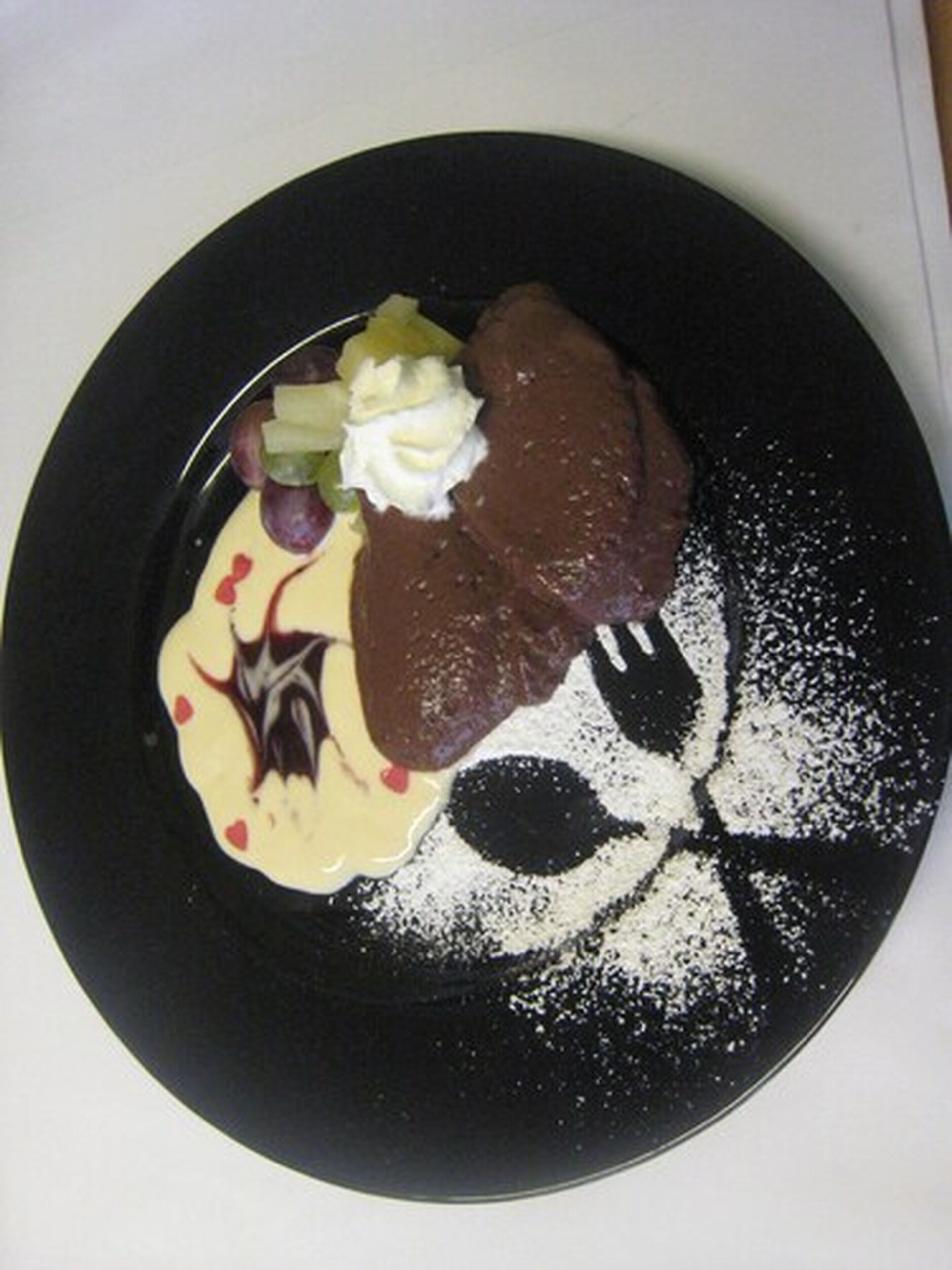 Un plat de postres amb pastís de xocolata, nata i fruita sobre un plat negre.