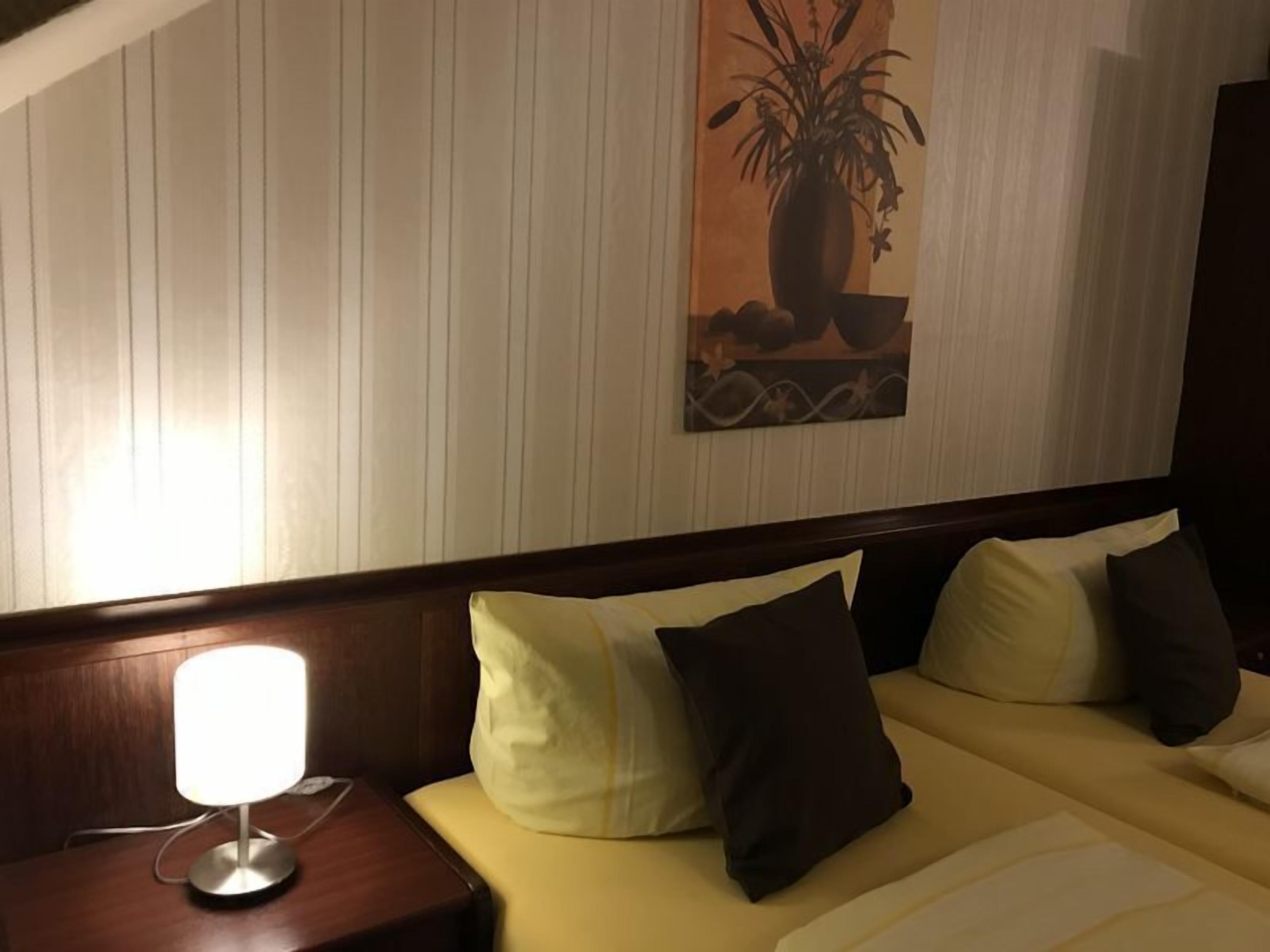 Ett hotellrum med en säng, ett nattduksbord med en lampa och en tavla som hänger på väggen.