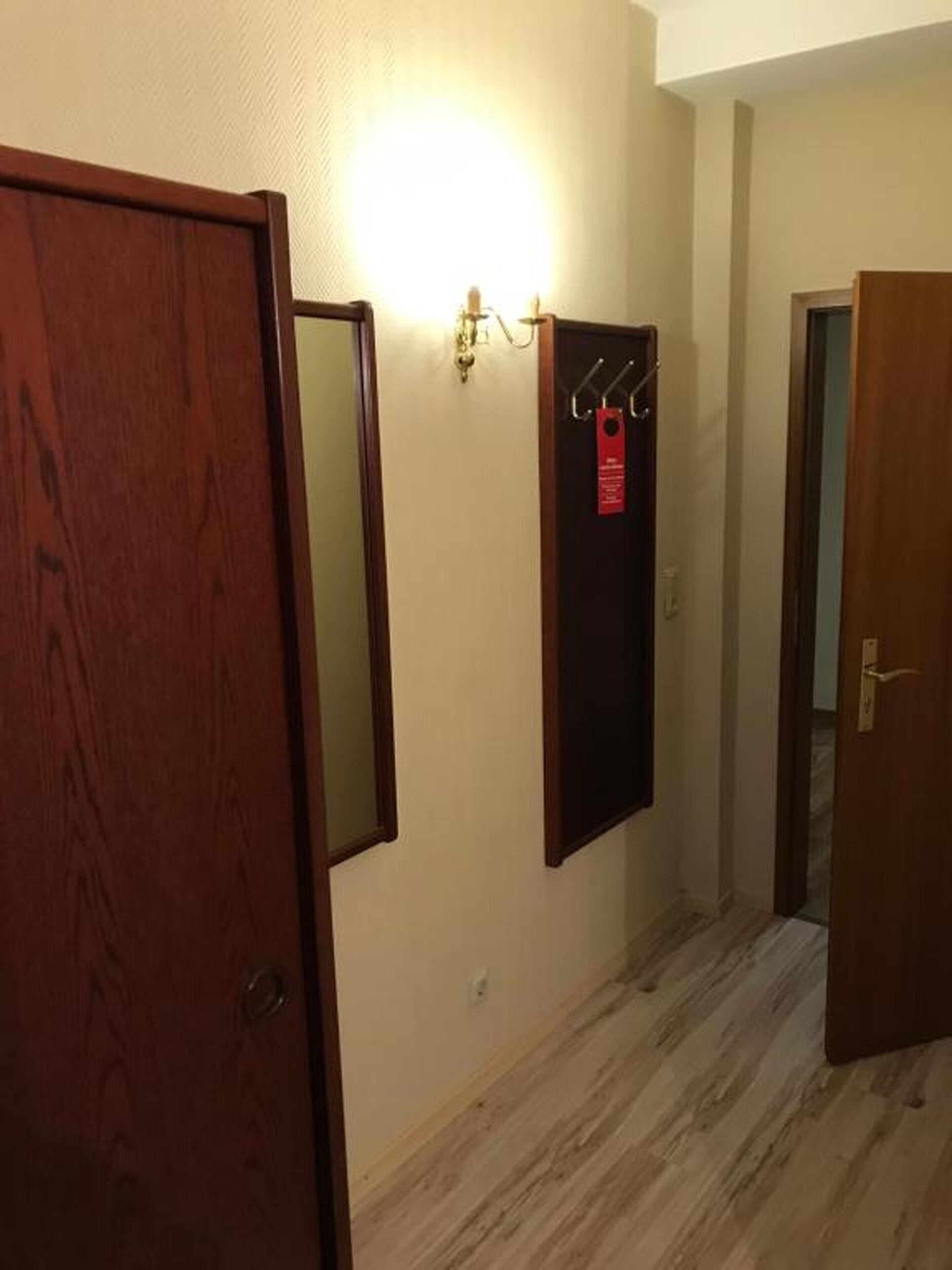 Un pasillo con puertas de madera, una lámpara de pared y un perchero con una etiqueta roja.
