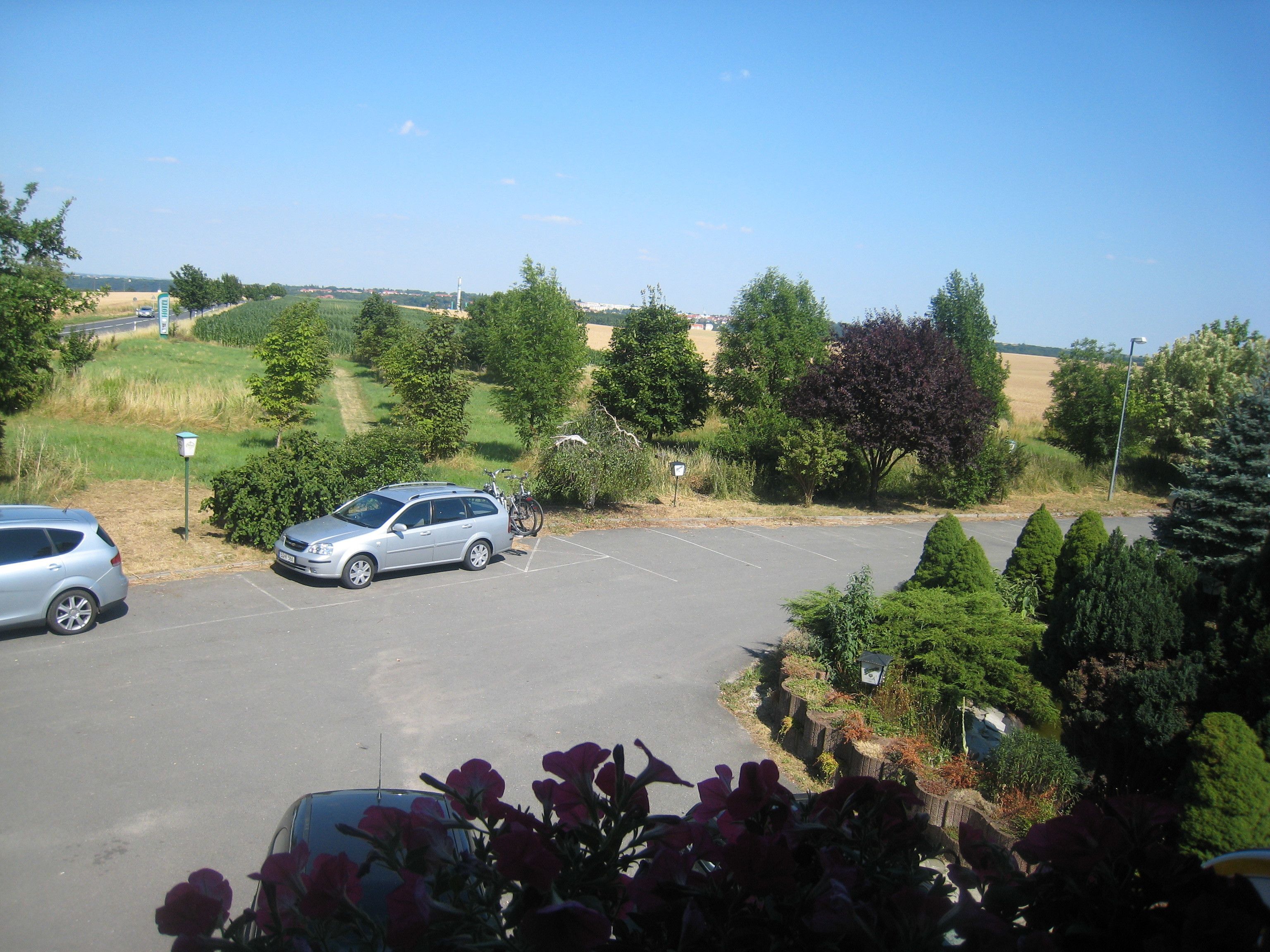 Ein Parkplatz mit zwei Autos und Fahrrädern, umgeben von Grünflächen und blauem Himmel.