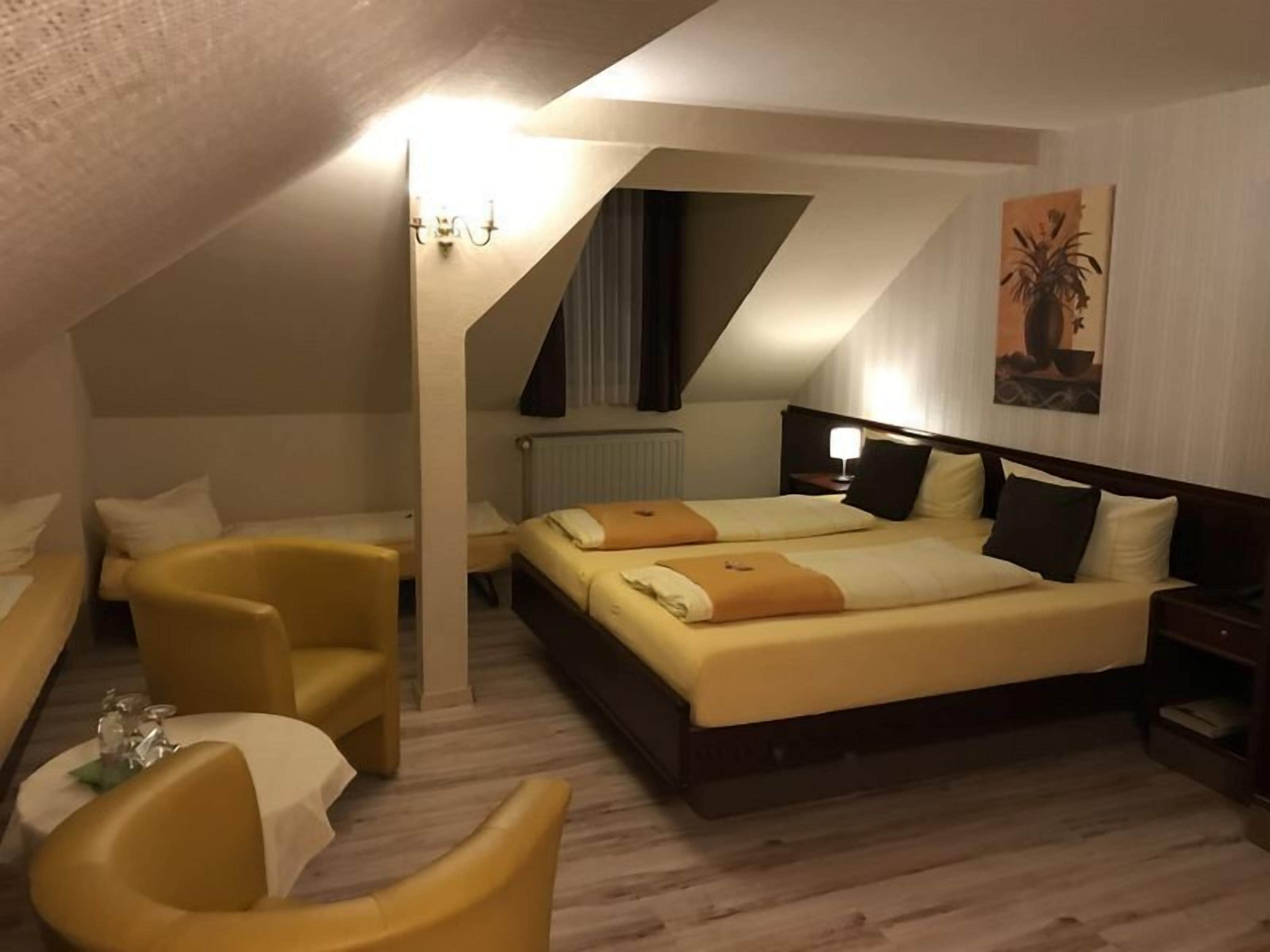 A hotel room with a large bed, two bedside tables, a chair, and a small table with a lamp.
