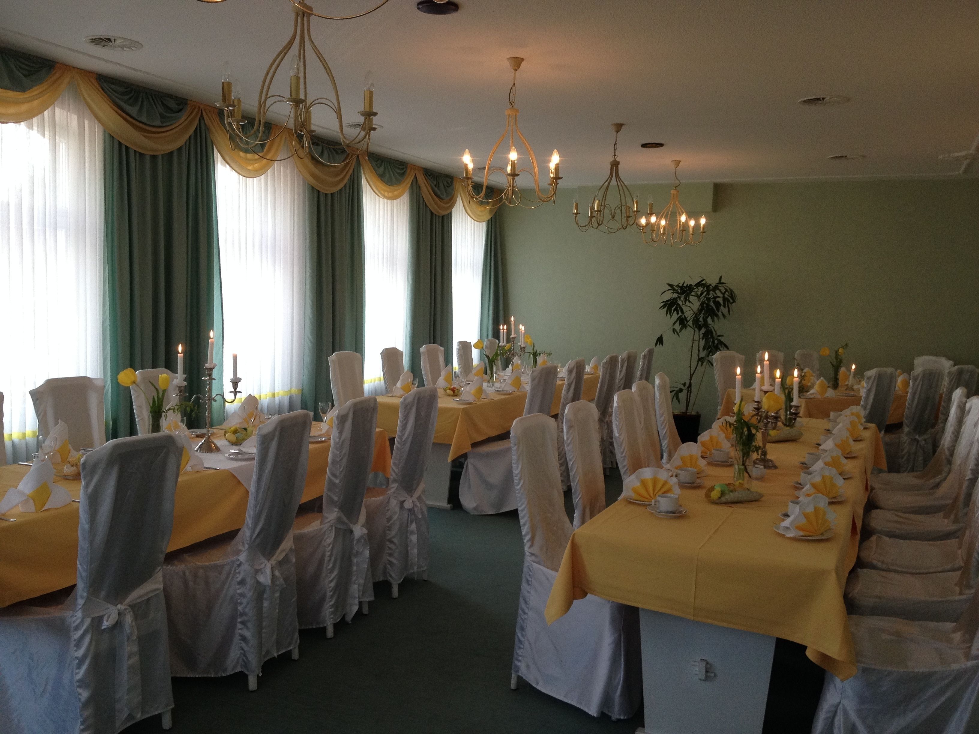Une salle de banquet avec des tables rondes, des chaises, des lustres et des rideaux drapés.