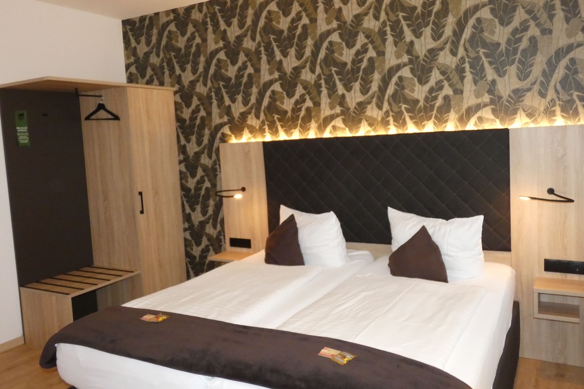 Une chambre d’hôtel avec un lit, une armoire, un banc et un mur décoré de motifs.