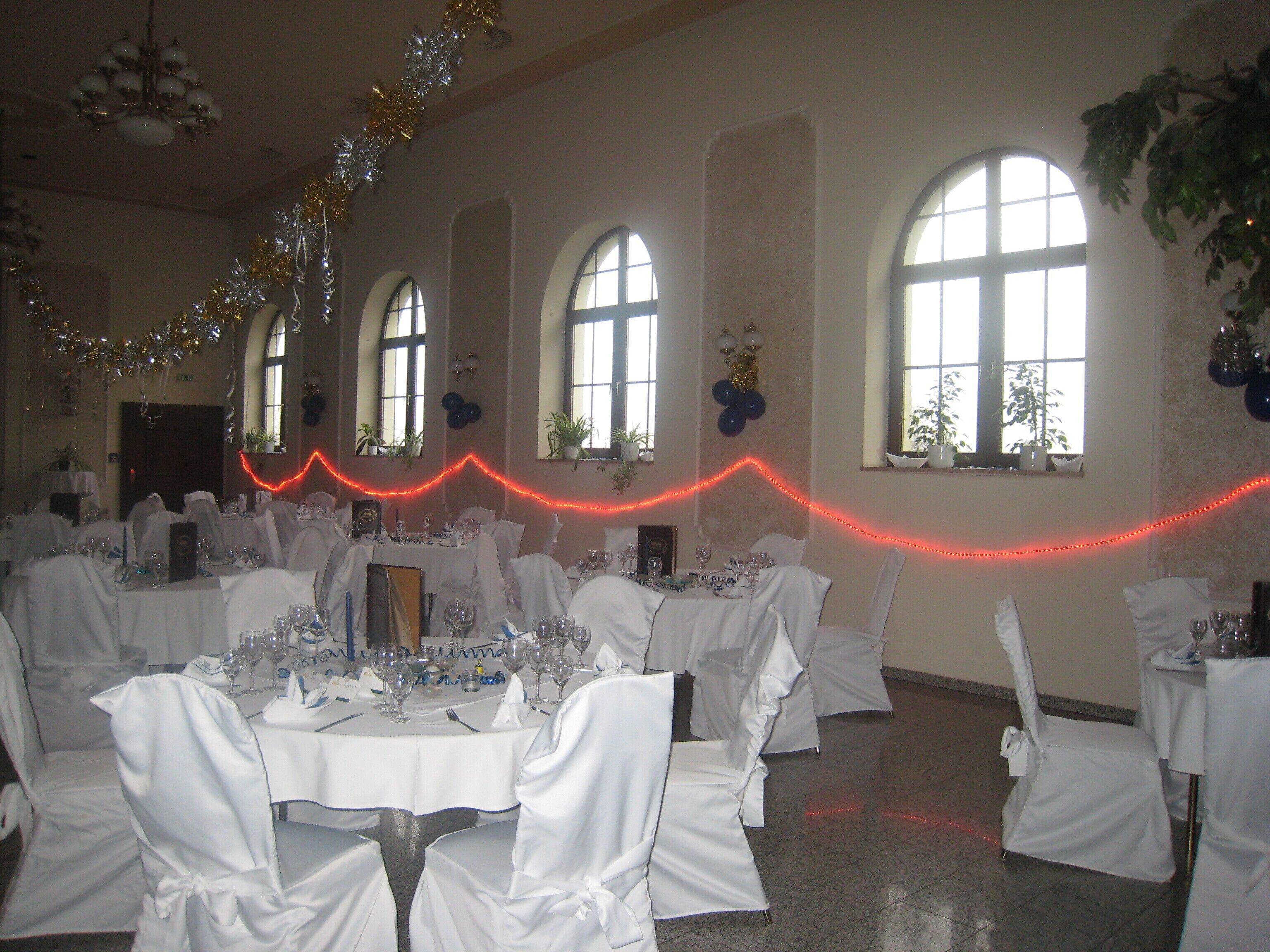 Un salón de banquetes con mesas dispuestas para un evento formal, con candelabros, ventanas amplias e iluminación decorativa.